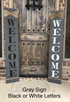 two wooden welcome signs sitting next to each other on top of a brick wall with the words, gray sign black or white letters