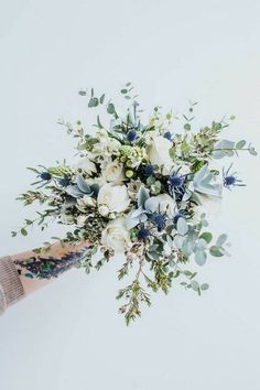 a bouquet of white and blue flowers is held by someone's hand