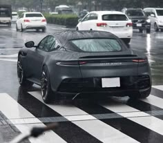 a black sports car driving down a street in the middle of traffic on a rainy day