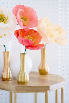 three vases with flowers in them sitting on a small table next to each other