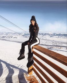 a woman sitting on top of a wooden bench in the snow