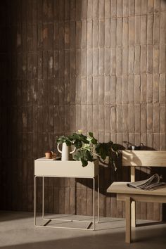 a table with a potted plant on it next to a wooden bench and wall