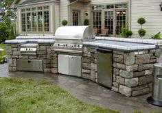 an outdoor kitchen with grills, sink and trash can