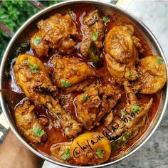 a person holding a metal bowl filled with chicken and peppers on top of a table