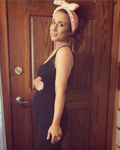 a woman standing in front of a door wearing a black top and pink headband