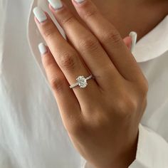 a woman's hand with white nails and a ring on her left hand, wearing a white shirt