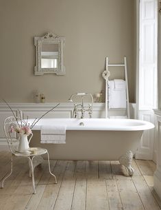 a white bath tub sitting in a bathroom next to a mirror and chair with flowers on it