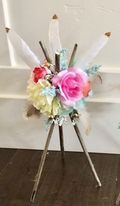 an arrangement of feathers, flowers and feathers in a vase on a wooden floor next to a wall