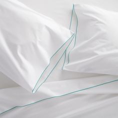 two white pillows with green piping on top of each pillowcase and one is made up