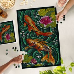 two pieces of art work on a table with flowers and leaves around it, one is goldfish and the other is green