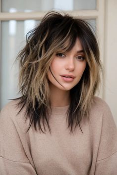 Woman with a shaggy layered hairstyle and bangs, wearing a beige sweater. Choppy Edgy Hair, Medium Textured Haircut, Vibrant Highlights, Choppy Layered Haircuts, Bold Highlights, Wolf Cuts, Shaggy Layers, Wolf Cut Long, Rocker Hair