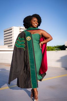 a woman in a green and black graduation gown posing for the camera with her hands on her hips