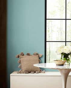 a white table and chair in front of a window with flowers on the bench next to it