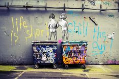 graffiti on the side of a building with two trash cans