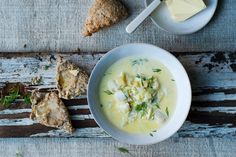 a bowl of soup next to some crackers on a wooden table with cheese and herbs