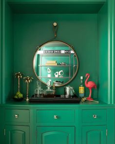 a green cabinet with a mirror and flamingo figurines on top in front of it