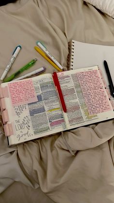 an open bible and some pens on a bed