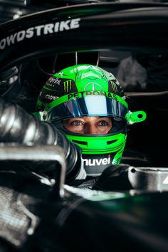 a man wearing a green helmet sitting in the drivers side of a race car with his eyes wide open