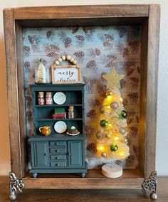 a miniature christmas tree in a wooden frame with lights on it and other decorations around the base