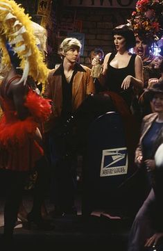 several people standing around in costumes and hats with one person holding a feathered hat