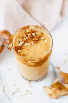 a glass with some food in it on top of a white table next to leaves