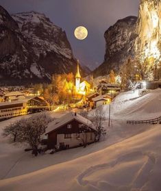 the full moon shines brightly over a small village on a snowy mountaintop with mountains in the background