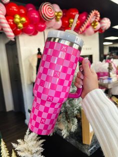 a person holding a pink and white checkered tumbler cup in front of christmas decorations