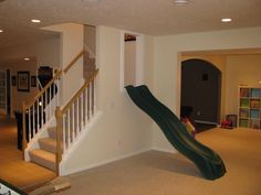 a slide in the middle of a living room next to a stair case and bookshelf