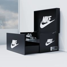 two boxes with nike logos on them sitting in front of a window, one opened and the other closed