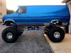 a blue truck with large tires parked in front of a building on the side of the road