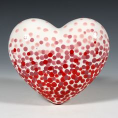 a red and white heart - shaped vase on a gray background with small dots in the center