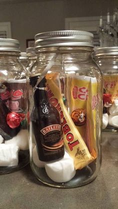 three glass jars filled with marshmallows, chocolate and other items on a counter