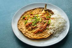 a white plate topped with food and rice on top of a blue tablecloth next to a fork