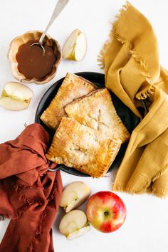 an apple pie is on a plate next to some apples and caramel sauces