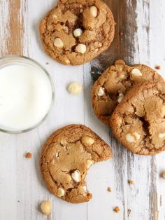 three cookies next to a glass of milk on a wooden table with white and brown speckles