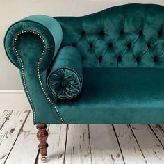 a green velvet couch with gold studding on the armrests and foot rest