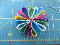 a close up of a flower made out of colored paper on a cutting board with a ruler