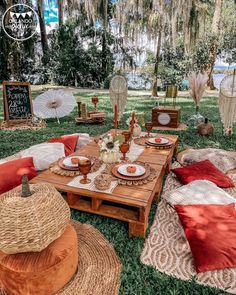 an outdoor seating area is set up with pillows, blankets and plates on the grass