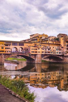 a bridge over a river with buildings on the other side and clouds in the sky