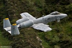 a fighter jet flying through the air with trees in the background