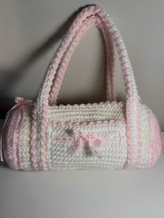 a crocheted white purse with pink trimmings and a bow on the handle