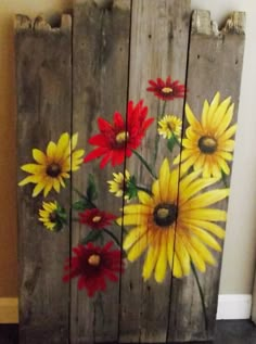 an old pallet painted with sunflowers and daisies on it is sitting in front of a wall