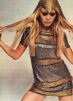 a woman with long blonde hair wearing a silver and gold dress, holding her hands on her hips