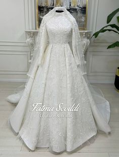 a white wedding gown with long sleeves and a high neckline is displayed in front of a mirror