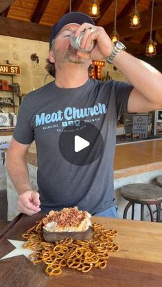 a man drinking from a can while standing in front of a table covered with pretzels