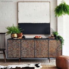 a black and gold sideboard with potted plants on it in front of a white brick wall