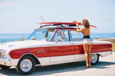 a woman standing next to a red and white car with surfboards on the roof