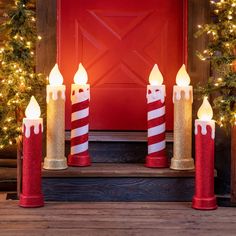 lighted candles in front of a red door with christmas wreaths and garland on it