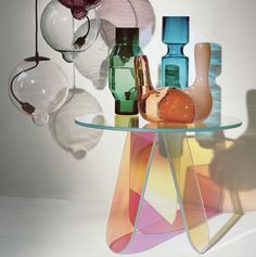 several vases and glass items on a table in front of a white wall with shadows