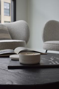 an open book on a table with a candle in front of it and two chairs behind it